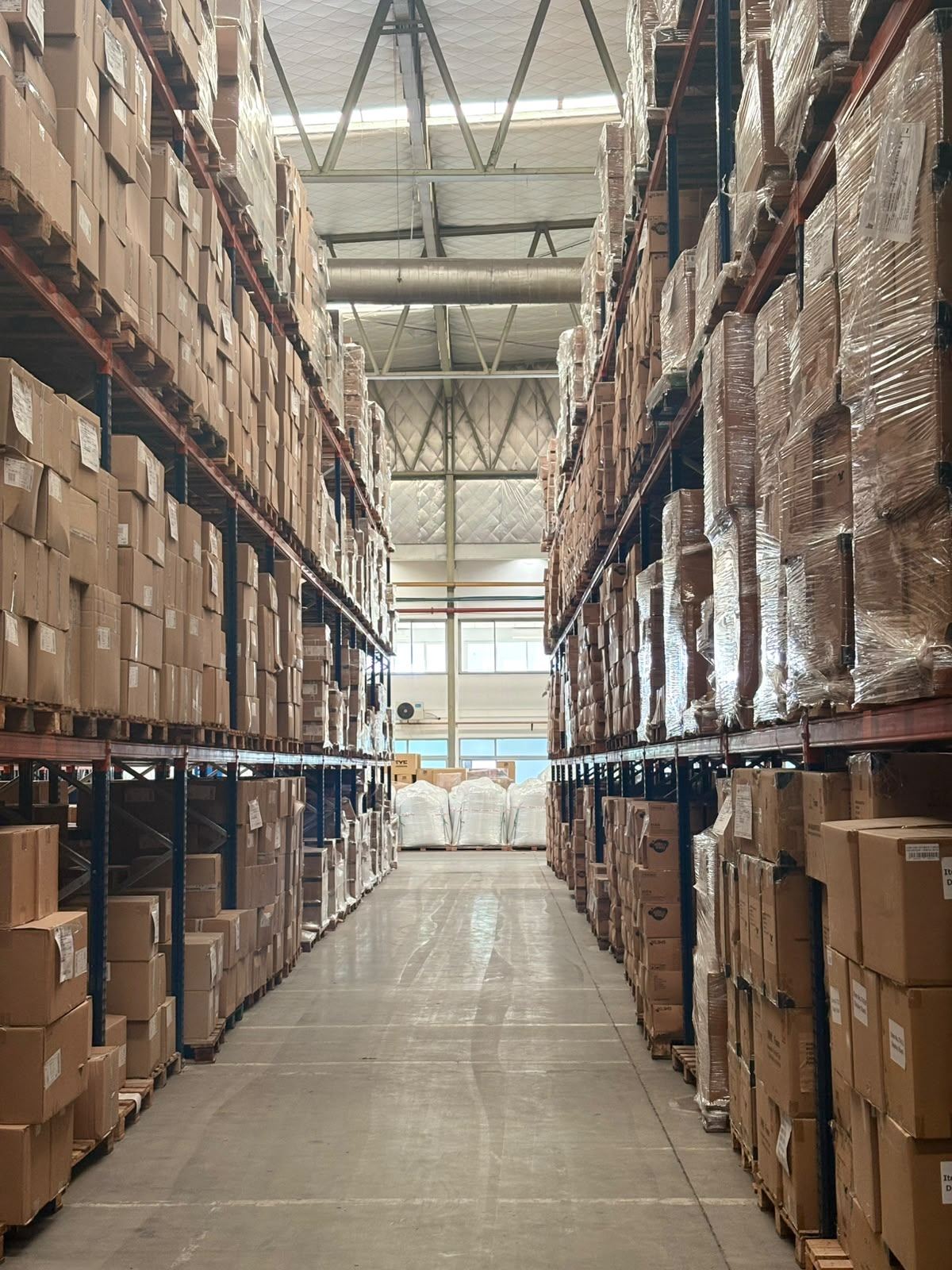 Pasillo entre racks con pallets de mercadería en el depósito de JB